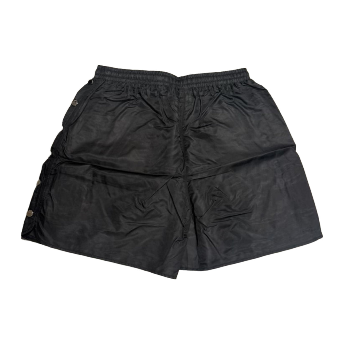 Back flat lay view of the black Saint Vanity technical nylon shorts, highlighting the lightweight athletic drape, a structured horizontal back yoke seam panel beneath the elastic waistband, and a clean, unadorned solid black reverse profile with subtle side-snap hardware visible at the margins.