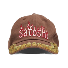Front view of the Satoshi Nakamoto hat in a washed brown cotton canvas, featuring pink embroidered 'Satoshi' text across the crown and a dense cluster of multi-sized brass and silver metal studs arranged across the brim to form a flame pattern.