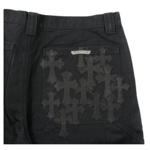 A close-up view of the back right pocket area, highlighting the intricate craftsmanship of roughly a dozen hand-stitched, tonal black premium leather signature cross patches layered dynamically over the heavy black canvas background, complete with a sterling silver brand scroll plaque anchored above the pocket seam.