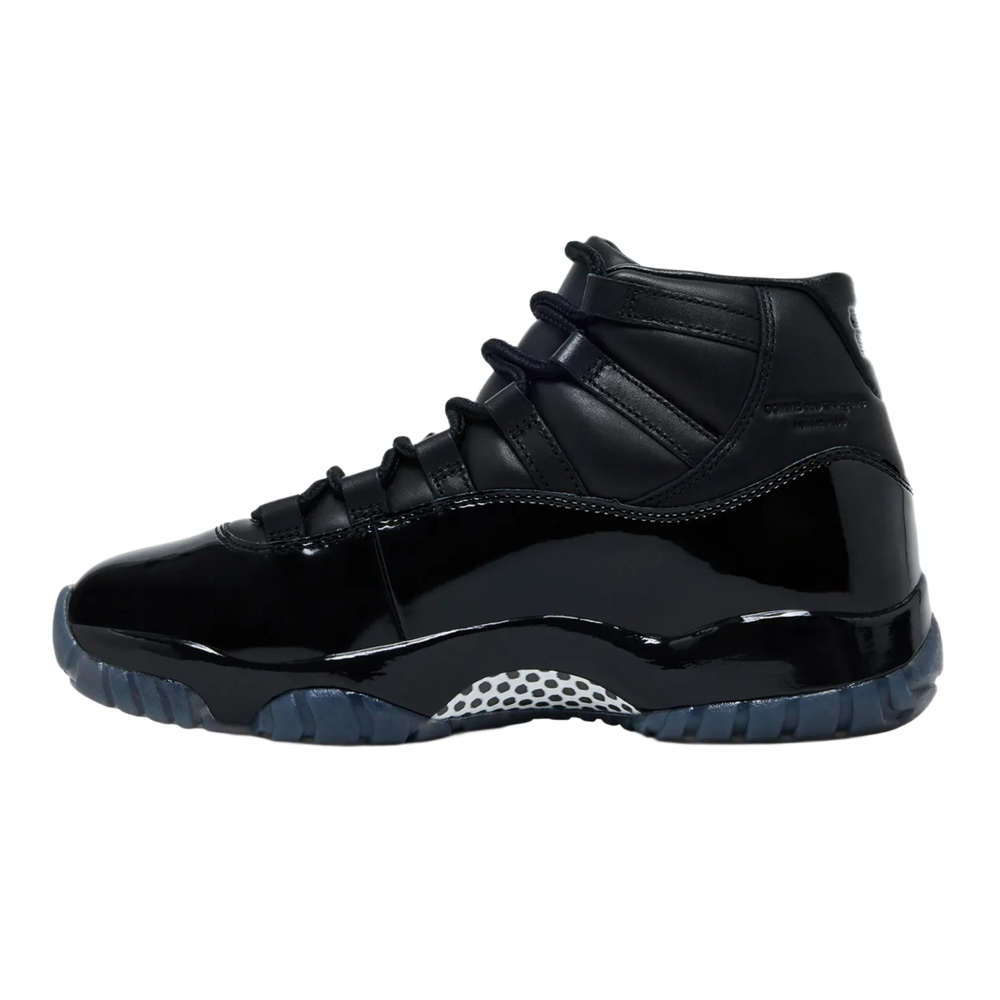 A clean lateral profile view of the all-black Jordan 11 x CDG sneaker against a dark background, showing the extended high-cut patent leather wrapping across a glossy Phylon midsole, accented by a white and black checkerboard carbon fiber shank plate beneath the arch.