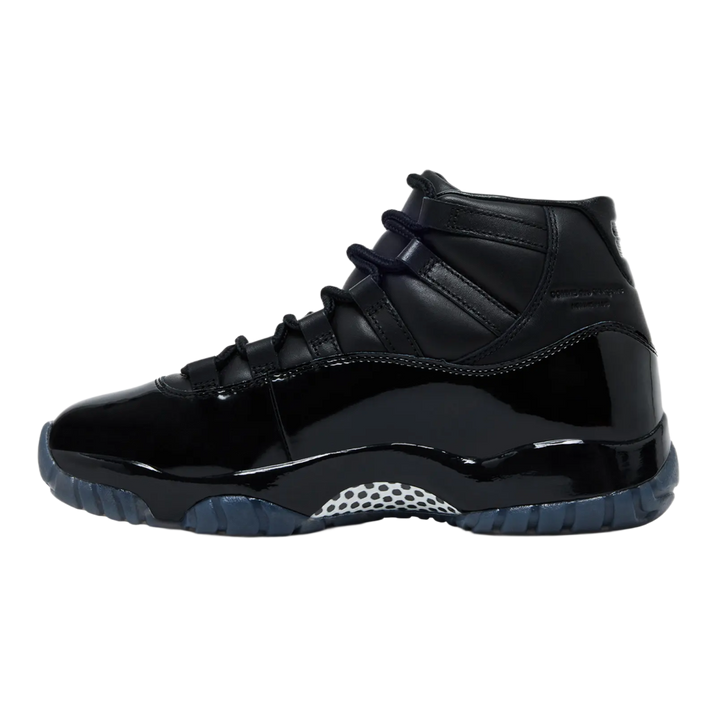 A clean lateral profile view of the all-black Jordan 11 x CDG sneaker against a dark background, showing the extended high-cut patent leather wrapping across a glossy Phylon midsole, accented by a white and black checkerboard carbon fiber shank plate beneath the arch.