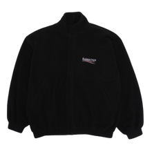Front flat lay view of the Balenciaga fleece jacket in a premium heavyweight plush jet-black polar fleece, showcasing a heavily padded oversized streetwear silhouette, a high mock-neck collar, a full-length center zipper track hidden beneath a clean fabric placket, loose dropped shoulders, relaxed sleeves with gathered elastic cuffs, and a small embroidered corporate political campaign wave logo monogram stitched cleanly in red, white, and blue on the left chest.