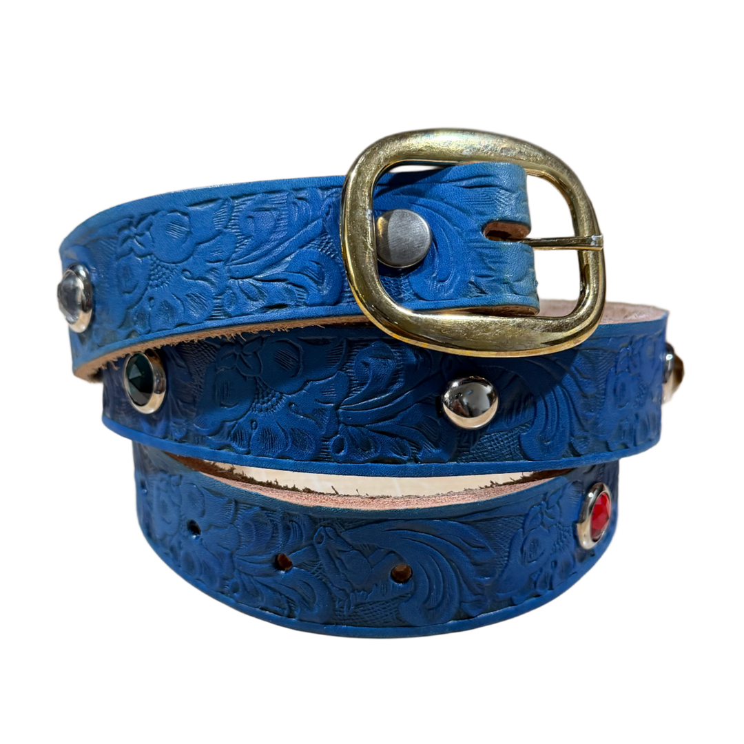 An overview of a coiled blue leather belt featuring a heavily textured grain strap decorated with debossed patterns and tiny circular metallic details, completed by a substantial, distressed antique brass roller buckle and matching brass rivets.