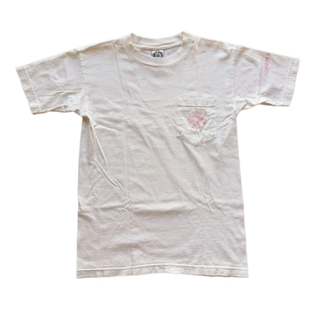 Front flat lay view of the vintage Chrome Hearts t-shirt in a soft, premium off-white or light cream cotton jersey knit, showcasing a relaxed boxy retro silhouette, a thick ribbed crewneck collar, an internal brand neck tag, a functional square patch pocket stitched on the left chest embellished with a signature floral cross monogram logo screen-printed in pastel pink, and a subtle pink script graphic hit detailed on the outer left sleeve.