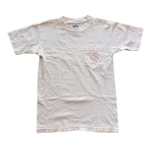 Front flat lay view of the vintage Chrome Hearts t-shirt in a soft, premium off-white or light cream cotton jersey knit, showcasing a relaxed boxy retro silhouette, a thick ribbed crewneck collar, an internal brand neck tag, a functional square patch pocket stitched on the left chest embellished with a signature floral cross monogram logo screen-printed in pastel pink, and a subtle pink script graphic hit detailed on the outer left sleeve.
