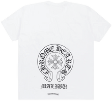 Back flat lay view of the white Chrome Hearts t-shirt, highlighting the clean streetwear drape, dominated by a large central black circular horseshoe logo graphic printed across the upper back panels with its classic signature cross motif inside, complemented by bold black gothic banner text reading 'MALIBU' curved directly underneath to denote its exclusive coastal boutique release provenance.