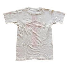 Back flat lay view of the cream vintage Chrome Hearts graphic t-shirt, highlighting the classic relaxed drape across the shoulders and a straight-cut lower hemline, dominated by a large, central pastel pink signature cemetery cross design motif screen-printed vertically down the center spine panel.