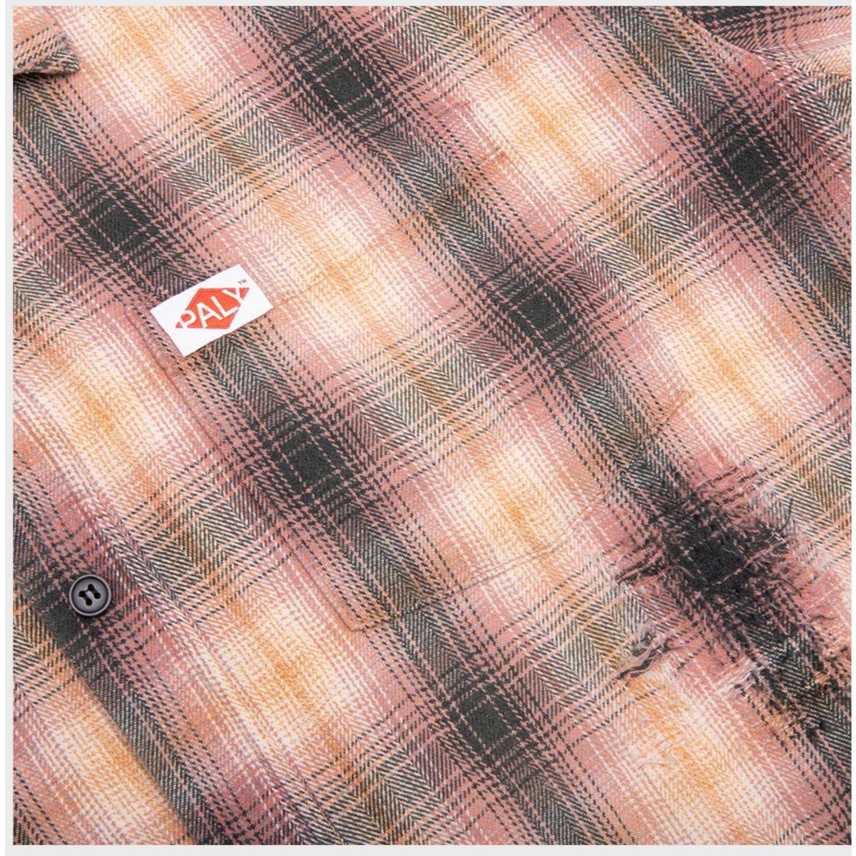 Macro detail of the left chest pocket area, highlighting the plaid fabric direction and a small, delicate red embroidered brand crest stitched onto the lower corner of the patch pocket.