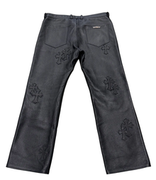 Back flat lay view of the black Chrome Hearts pebbled leather pants, showcasing the straight-leg silhouette with dual rear patch pockets, a silver scroll branding plaque on the right pocket, and a multi-layered arrangement of black leather cemetery cross patches stitched along the rear thighs and legs.