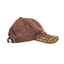 A right-side profile view of the washed brown Satoshi Nakamoto cap, highlighting the curved brim packed with multi-toned metal studs, a structured six-panel crown, and matching stitched ventilation eyelets.