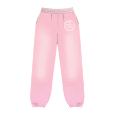 Front flat lay view of the Saint Vanity women's collegiate sweatpants in a soft pastel pink cotton fleece, showcasing a relaxed taper silhouette with gathered elastic ankle cuffs, a thick ruched elastic waistband with a matching tonal drawstring, and a circular white collegiate emblem graphic printed subtly on the upper left thigh.