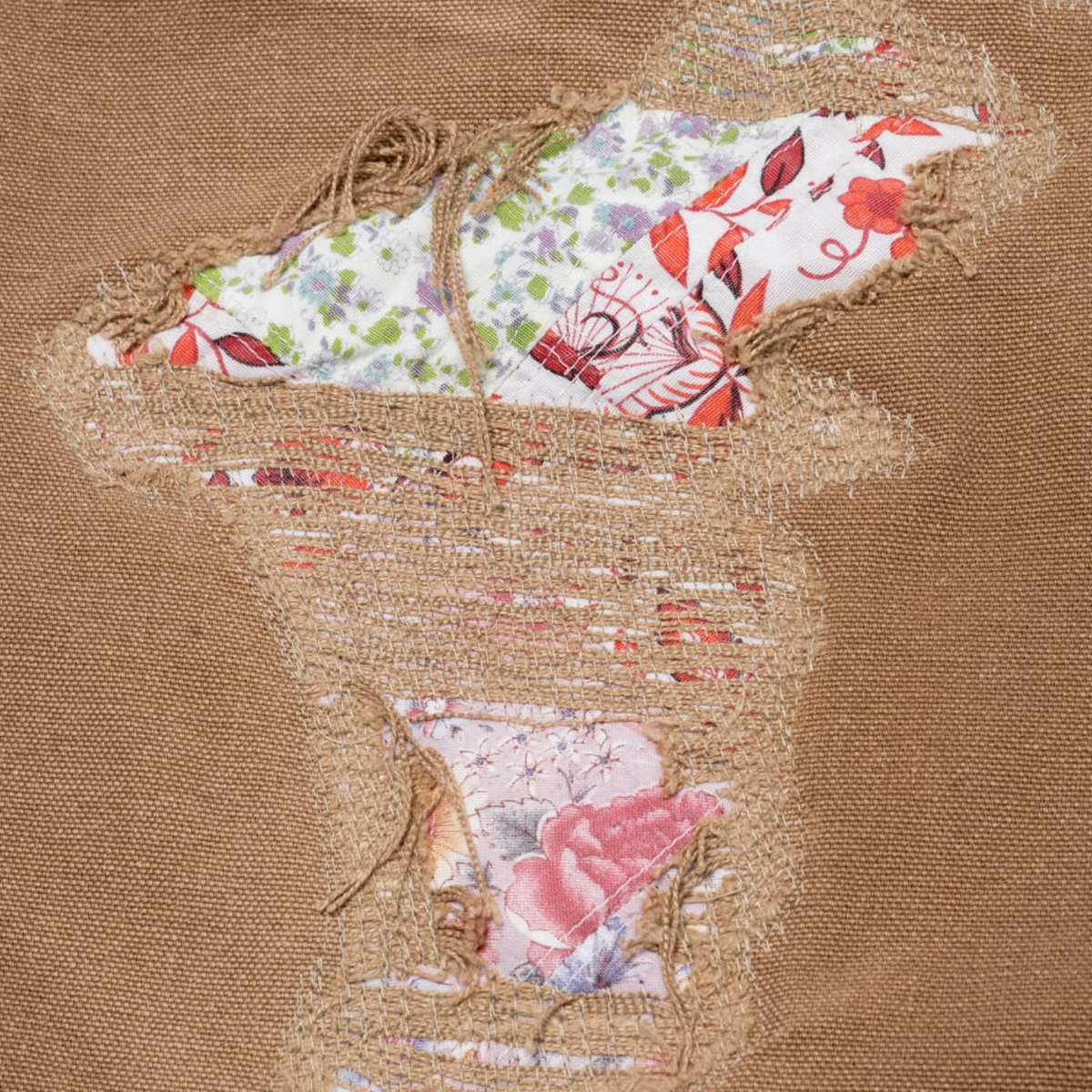 A close-up shot focusing on the lower left front thigh panel, highlighting a detailed, colorful printed graphic depicting a classical figurative artwork scene set against the raw, sun-faded texture of the brown duck canvas fabric.
