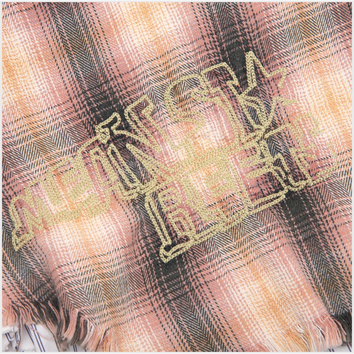 Close-up detail of the plaid fabric surface, showcasing a subtle, faded monochrome graphic overlay consisting of a fine lined checkerboard and gothic border artwork printed across the pattern fabric.