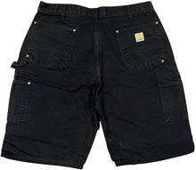 Back flat lay view of the black denim Carhartt carpenter shorts, showcasing two rear patch pockets with a woven Carhartt logo patch stitched onto the right pocket, alongside multi-layered tool utility pockets on the right thigh.