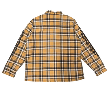 Back flat lay view of the tan plaid Chrome Hearts flannel shirt jacket, highlighting the clean pattern alignment across the rear yoke and lower back panels, dominated by a large, intricate black screen-printed graphic emblazoned across the upper back torso depicting a circular horseshoe layout of signature brand lettering framing an oversized gothic floral cross design motif.