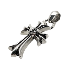 A three-quarter angled profile view of the sterling silver heart cross pendant resting flat, emphasizing the heavy architectural thickness and sculptural depth of the flared cross arms, the deep black oxidized recesses of the central heart design, and the high-polish sheen of the metal facets.