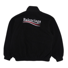Back flat lay view of the black Balenciaga fleece jacket, highlighting the loose streetwear volume and thick plush insulating pile running uniformly across the back panel and hemline, dominated by a large matching multi-colored embroidered political campaign wave logo emblazoned boldly across the upper back shoulders.