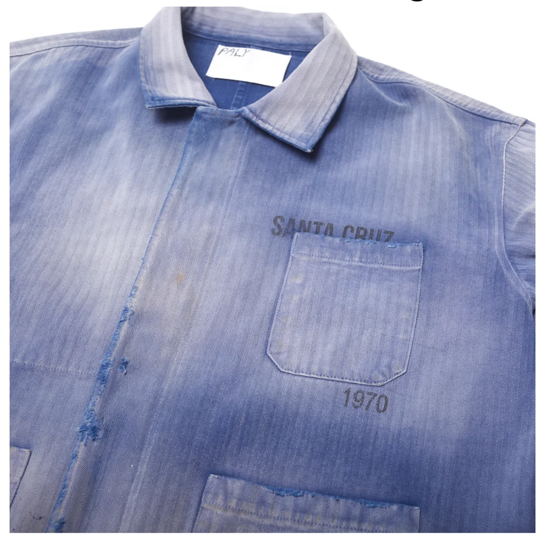 Close-up front detail of the Paly Work Shirt collar and top pocket, showing the textured herringbone cotton canvas, distressed raw-edge placket seams, and a dark 'SANTA CRUZ 1970' stamp.