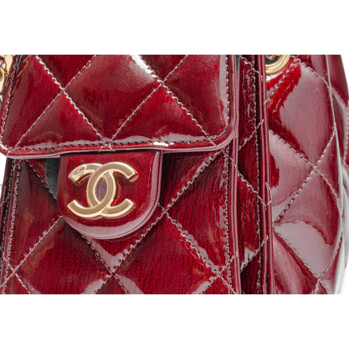 An extreme macro shot focusing on the quilted leather panels, highlighting the rich, fine-grain crinkle lines and natural leather wrinkles that give the shiny burgundy calfskin surface its distinctive textured and light-reflective depth.