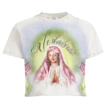 Front flat lay view of the Vertabrae 'Prayers' t-shirt in a washed cream cotton jersey knit, highlighting an all-over custom airbrushed layout featuring neon green and sand-tan cloud-like halo gradients, a thick ribbed crewneck collar with a dark internal brand tag, and a large central multi-colored graphic illustration of a praying religious figure, crowned by stylized arched cursive typography reading 'Vertabrae' screen-printed cleanly across the chest.