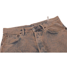 Macro detail of the oil-washed denim fabric surface, displaying the multi-toned brown, tan, and blue wash variations alongside the precise perimeter topstitching.