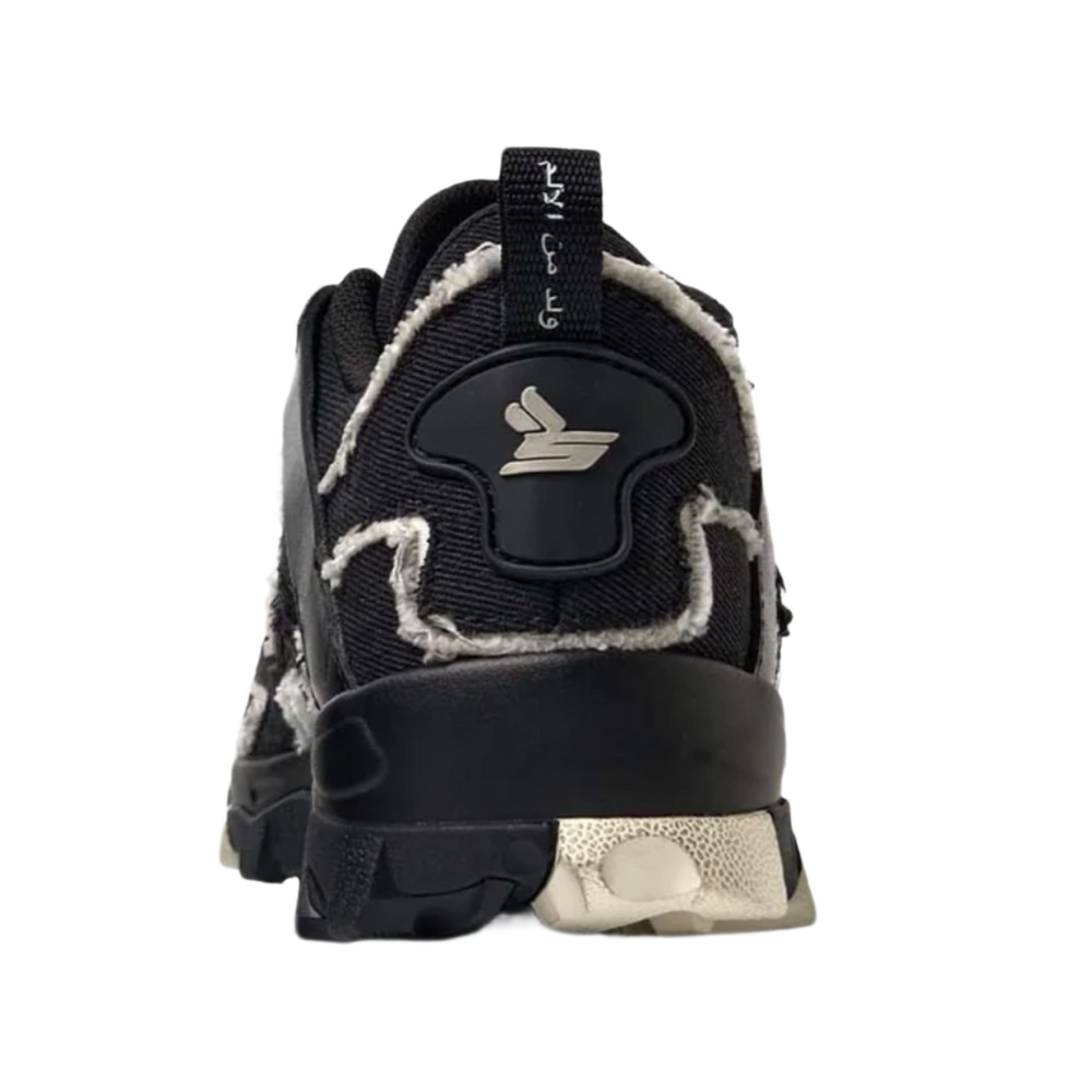 A straight-on rear view of the black Sicko Vessel trail shoe resting flat, highlighting the robust structural heel counter paneling, contrasting metallic silver or light grey technical accents along the rear heel wrap, a centered vertical canvas pull loop, and the thick, protective lugged footprint of the black rubber rugged outsole.