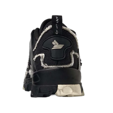 A straight-on rear view of the black Sicko Vessel trail shoe resting flat, highlighting the robust structural heel counter paneling, contrasting metallic silver or light grey technical accents along the rear heel wrap, a centered vertical canvas pull loop, and the thick, protective lugged footprint of the black rubber rugged outsole.