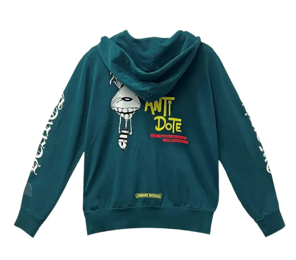 Front flat lay view of the Chrome Hearts x Matty Boy 'Antidote' zip-up hoodie in a premium heavyweight teal-green cotton fleece, showcasing a structured boxy streetwear silhouette, a high-neck drawstringless hood, a polished silver metal center zipper track, split front kangaroo pouch pockets, a yellow and black collaborative cartoon checkerboard motif printed on the left chest, and bold white gothic script reading 'CHROME' down the right sleeve and 'HEARTS' down the left sleeve in a heavy screen-print.