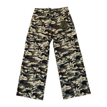 Front flat lay view of the Saint Vanity cargo pants in a textured woodland camouflage nylon fabric, showcasing a relaxed straight-leg utility silhouette, an integrated elastic waistband, deeply inset side slip pockets, and low-profile rectangular cargo utility pockets stitched along both outer thighs with a small contrasting green embroidered patch applied to the left pocket flap.