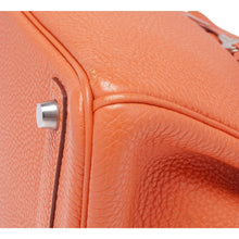 A macro detail shot of a lower base corner, highlighting the impeccable hand-stitching, clean resin edge coating, and the premium quality of the grained orange leather.