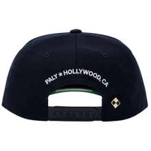 A straight-on rear view of the navy blue Paly canvas cap resting flat, highlighting the low-profile crown posture and uniform panels, featuring an adjustable fabric strap closure with a metallic slider buckle, accented cleanly by white embroidered branding text reading 'PALY HOLLYWOOD CA.' stitched across the rear opening arc.