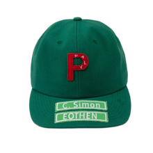 A straight front studio layout view of the Paly 'P' cap, showcasing a structured six-panel profile crafted from a premium emerald green cotton twill canvas, featuring a curved stitched brim, a matching green top button, and a large bold red embroidered letter 'P' motif on the center crown, complemented on the lower brim by two stacked rectangular fabric patches with contrast borders reading 'C. Simon' and 'EOTHEN'.