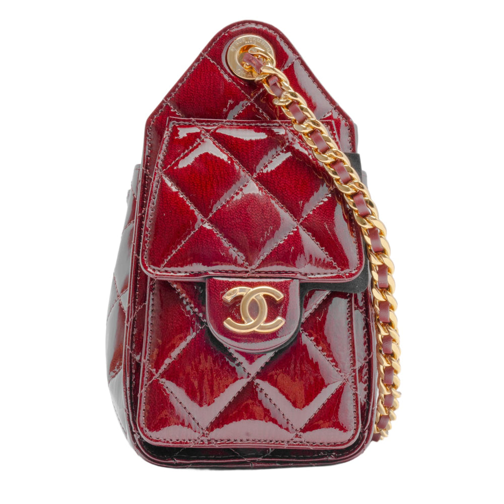 A straight-on front profile view of the dark burgundy quilted leather hobo bag hanging vertically, emphasizing its deep architectural slouch, the reflective high-gloss sheen of the shiny calfskin material, and the perfect symmetrical alignment of the gold interwoven chain straps draped over the top.