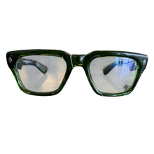 A centered, straight-on front view of the Chrome Hearts 'Gnarlin' glasses, showcasing the thick translucent olive-green acetate frame, clear lenses with a signature laser-etched floral emblem, and small silver accents at the upper corners.