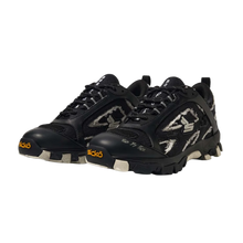 A three-quarter lateral angled layout view of both black Sicko Vessel hiking shoes arranged together, emphasizing the aggressive geometric shapes of the layered side panels, the protective toe cap bumpers, the complex technical lacing matrix, and the dense, multi-textured performance materials used across the upper design.