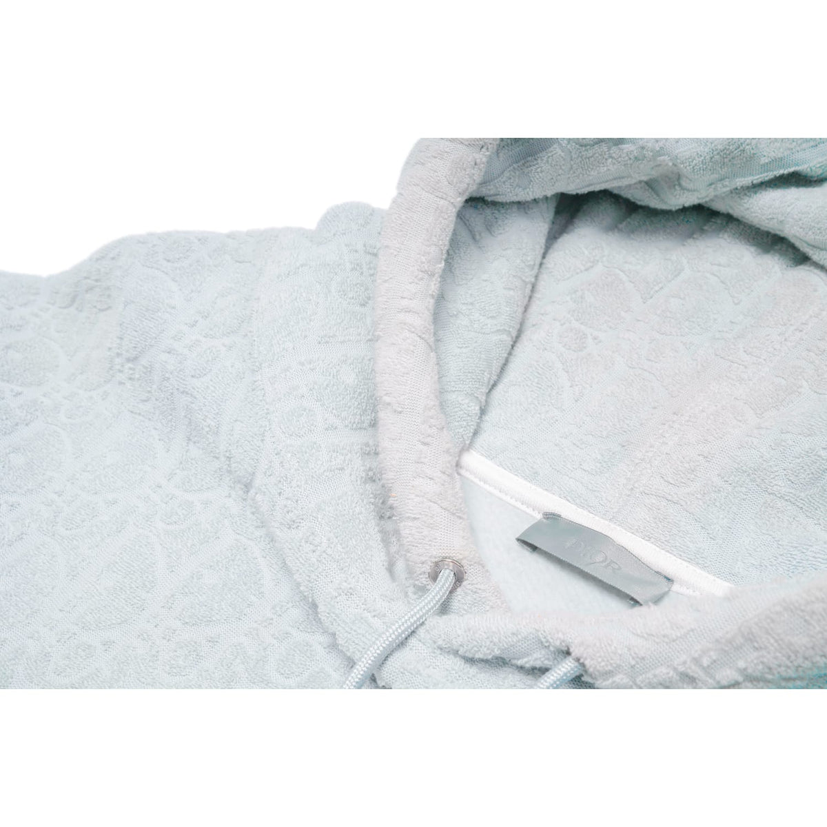 Close-up view of the interior collar neckline, highlighting the plush texture of the light blue towel cotton fabric, a white woven 'DIOR' brand label, and natural sun-faded discoloration around the inner hood seams.