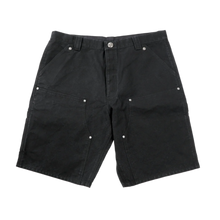 Front flat lay view of the Chrome Hearts carpenter shorts in heavy structured black cotton duck canvas, showcasing a relaxed knee-length utility silhouette, reinforced double-layer front knee panels secured with silver metallic rivets, classic slash side pockets, and a signature sterling silver button closure at the waistband.