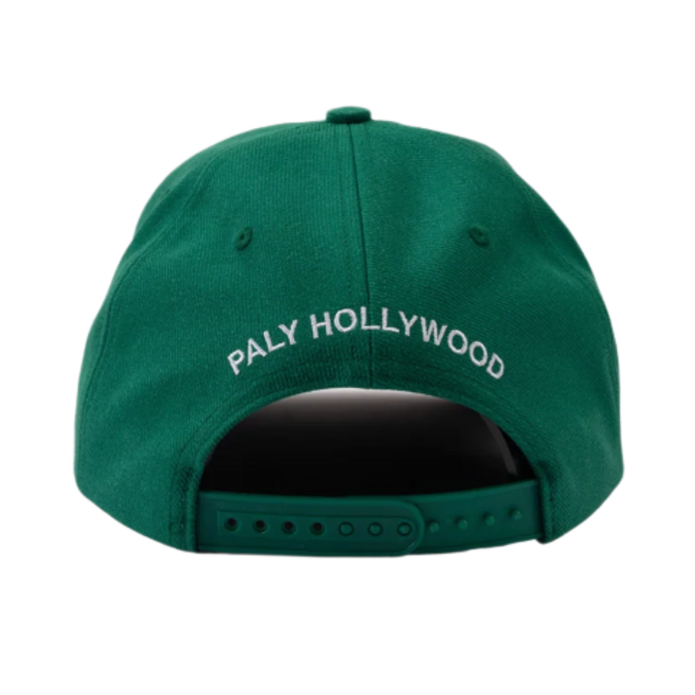 A straight-on rear view of the emerald green Paly twill cap resting flat, highlighting the curved crown architecture, tonal ventilation eyelets, and an adjustable green fabric strap closure with a metallic adjustment buckle, accented cleanly by arched white embroidered branding text reading 'PALY HOLLYWOOD' stitched across the rear panel section.
