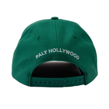 A straight-on rear view of the emerald green Paly twill cap resting flat, highlighting the curved crown architecture, tonal ventilation eyelets, and an adjustable green fabric strap closure with a metallic adjustment buckle, accented cleanly by arched white embroidered branding text reading 'PALY HOLLYWOOD' stitched across the rear panel section.