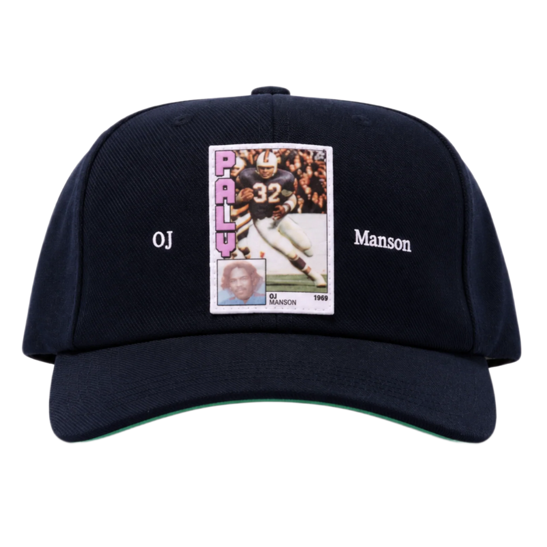 A straight front studio layout view of the Paly 'OJ Manson' hat, showcasing an unstructured six-panel vintage dad hat profile crafted from a premium washed navy blue cotton twill canvas, featuring a curved stitched brim, a centralized rectangular photo-graphic panel patch screen-printed on the front crown depicting an athletic sports trading card image, flanked on either side by minimal white printed script reading 'OJ' and 'Manson'.