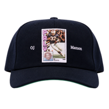 A straight front studio layout view of the Paly 'OJ Manson' hat, showcasing an unstructured six-panel vintage dad hat profile crafted from a premium washed navy blue cotton twill canvas, featuring a curved stitched brim, a centralized rectangular photo-graphic panel patch screen-printed on the front crown depicting an athletic sports trading card image, flanked on either side by minimal white printed script reading 'OJ' and 'Manson'.