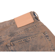 Close-up view of the upper back right waistband, highlighting the signature Acne Studios minimalist pink leather logo patch stitched over the textured, distressed brown denim.