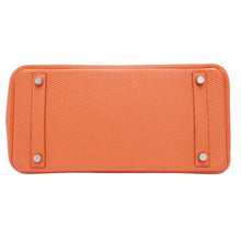 A bottom view of the base of the orange Hermès Birkin 30 bag, showcasing the protective rectangular leather paneling and four silver palladium feet studs.