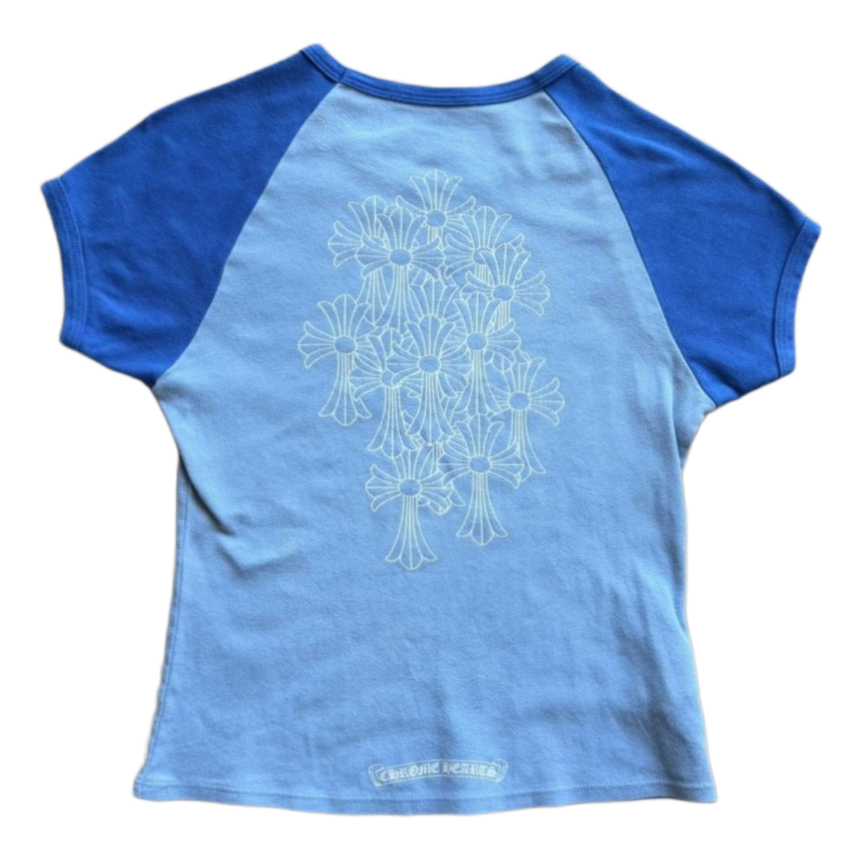 Back flat lay view of the two-tone blue vintage Chrome Hearts baby tee, highlighting the cropped streetwear proportions and sporty raglan sleeve seams across the upper shoulders, dominated by a large, central tonal graphic screen-printed across the back torso depicting an intricate gothic cemetery cross cluster arrangement.