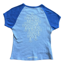 Back flat lay view of the two-tone blue vintage Chrome Hearts baby tee, highlighting the cropped streetwear proportions and sporty raglan sleeve seams across the upper shoulders, dominated by a large, central tonal graphic screen-printed across the back torso depicting an intricate gothic cemetery cross cluster arrangement.