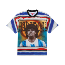 Front flat lay view of the Supreme short-sleeve soccer jersey featuring a vibrant multicolor design with blue, white, and orange horizontal stripes, completed by a black v-neck collar and a massive central portrait graphic of Diego Maradona.