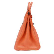 A right profile view of the orange Hermès Birkin bag, displaying the uniform pebbled leather texture and the architectural structure of the side panel folds.