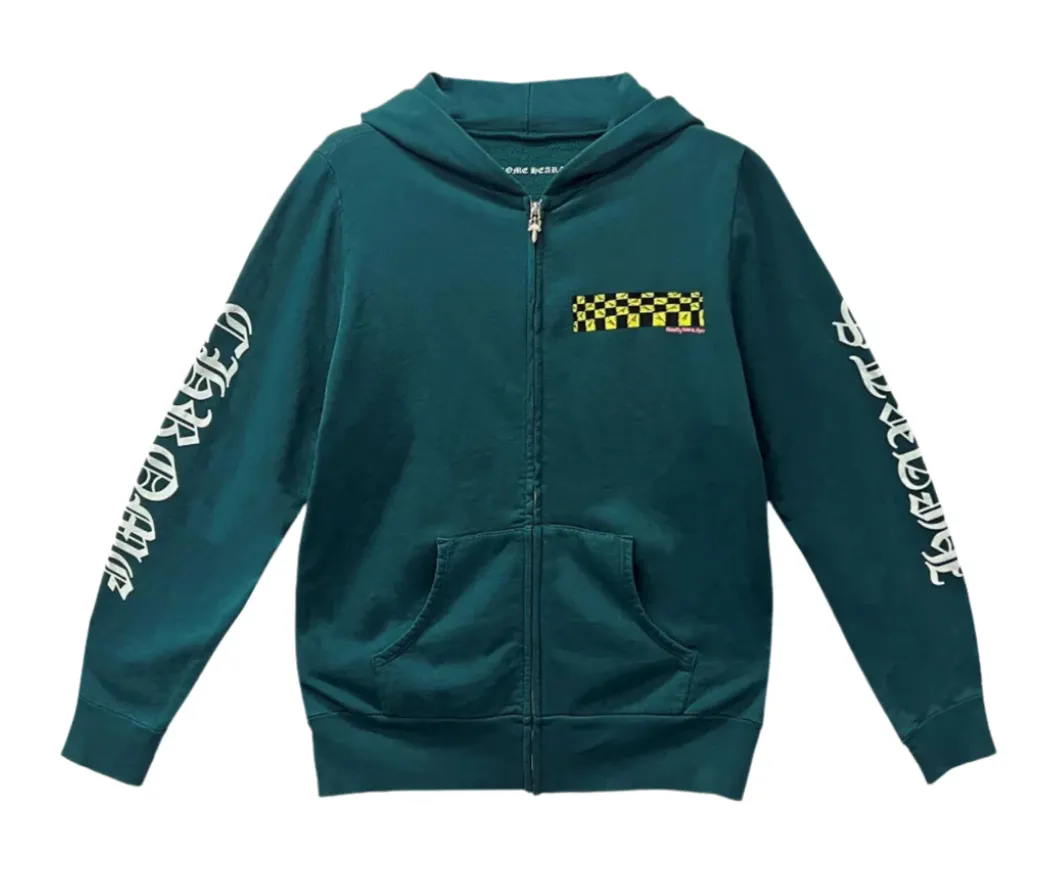 Front flat lay view of the Chrome Hearts x Matty Boy 'Antidote' zip-up hoodie in a premium heavyweight teal-green cotton fleece, showcasing a structured boxy streetwear silhouette, a high-neck drawstringless hood, a polished silver metal center zipper track, split front kangaroo pouch pockets, a yellow and black collaborative cartoon checkerboard motif printed on the left chest, and bold white gothic script reading 'CHROME' down the right sleeve and 'HEARTS' down the left sleeve in a heavy screen-print.