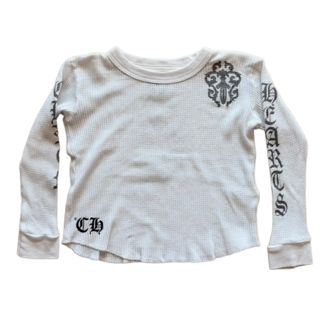 Front flat lay view of the Chrome Hearts vintage kids long-sleeve thermal top in a light baby blue or off-white waffle-knit cotton, showcasing a relaxed crewneck silhouette, tight ribbed cuffs, a black gothic 'CH' monogram printed on the lower right hip, and bold black gothic scroll lettering running down the length of the left sleeve flanked by a stylized cemetery cross motif on the left shoulder.