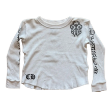 Front flat lay view of the Chrome Hearts vintage kids long-sleeve thermal top in a light baby blue or off-white waffle-knit cotton, showcasing a relaxed crewneck silhouette, tight ribbed cuffs, a black gothic 'CH' monogram printed on the lower right hip, and bold black gothic scroll lettering running down the length of the left sleeve flanked by a stylized cemetery cross motif on the left shoulder.